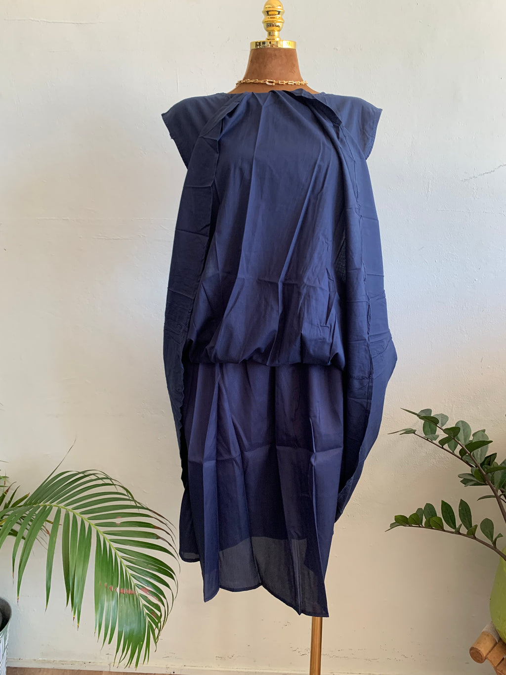 Navy blue dress on a mannequin against a white background with green plants.